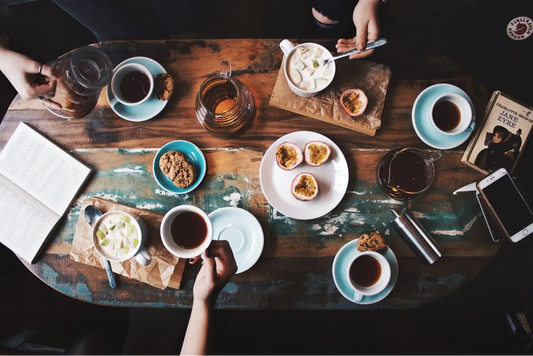 table en bois avec quatre personnes autour qui boivent à la fois du thé et du café dans des tasses