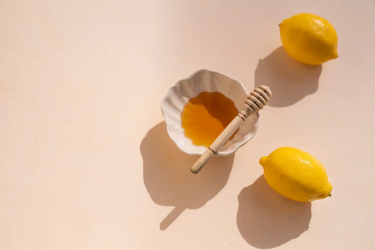 récipient de miel avec deux citrons à côté posés sur une table