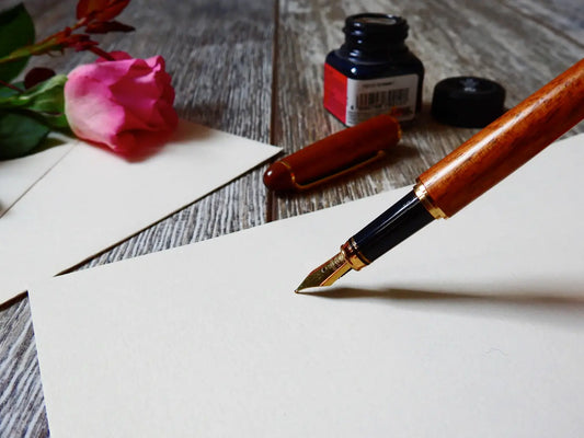 stylo plume prêt à écrire sur une feuille blanche avec une rose dans le fond sur un bureau en bois