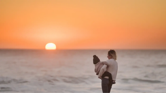 une maman avec son enfant dans ses bras sur la plage devant un beau coucher de soleil