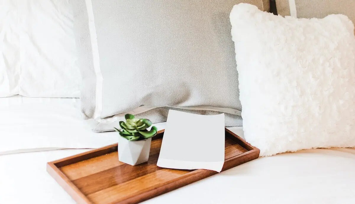 cahier blanc sur une table de lit en bois posé sur un lit avec des draps blancs